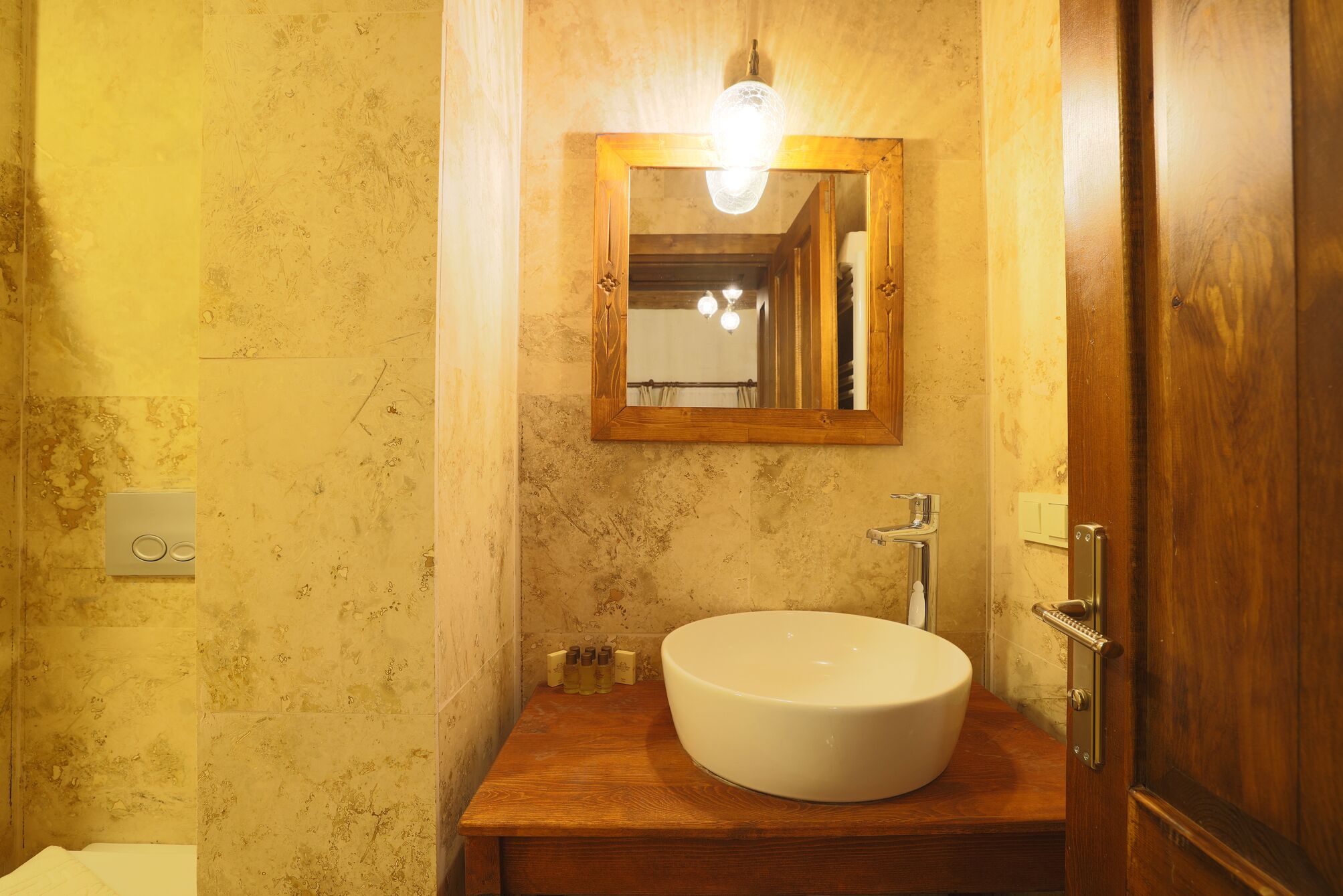 A bathroom with a wooden vanity, a white sink, a mirror, and a light fixture above the mirror.