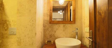 A bathroom with a wooden vanity, a white sink, a mirror, and a light fixture above the mirror.