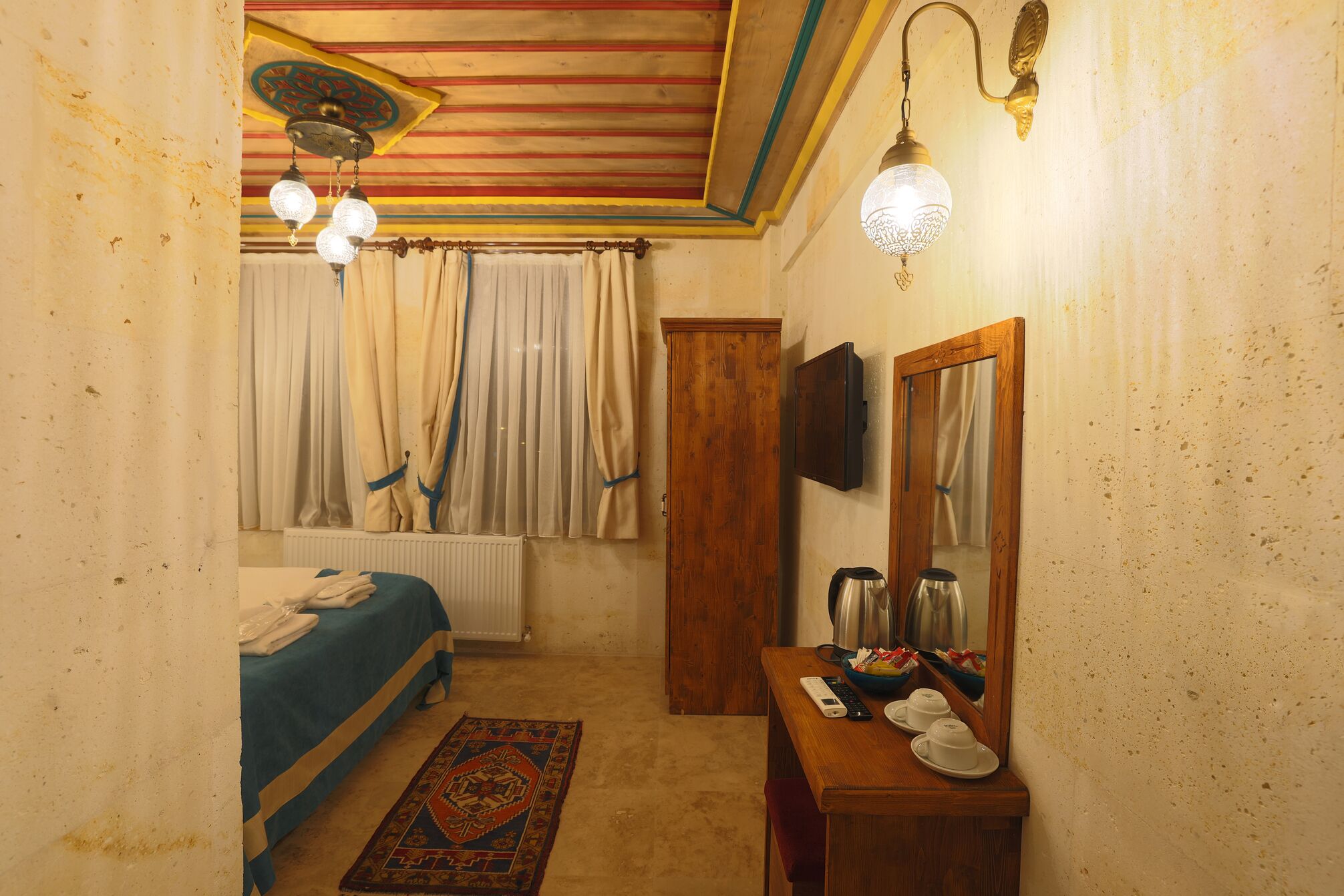 Une chambre à coucher comprenant un lit, une commode en bois, un radiateur, un miroir et un téléviseur fixé au mur.