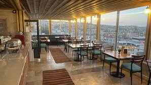 A restaurant with a high ceiling and large windows offering a city view.