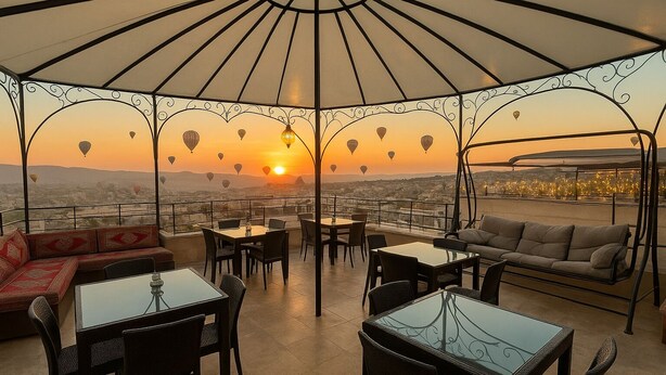 An outdoor terrace with a glass table and chairs, a sofa, and a hanging chair, all under a large umbrella.