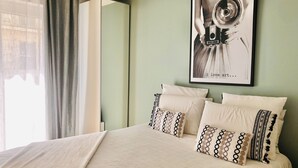 A neatly made bed with patterned pillows, a framed artwork on the wall, and a window with curtains.