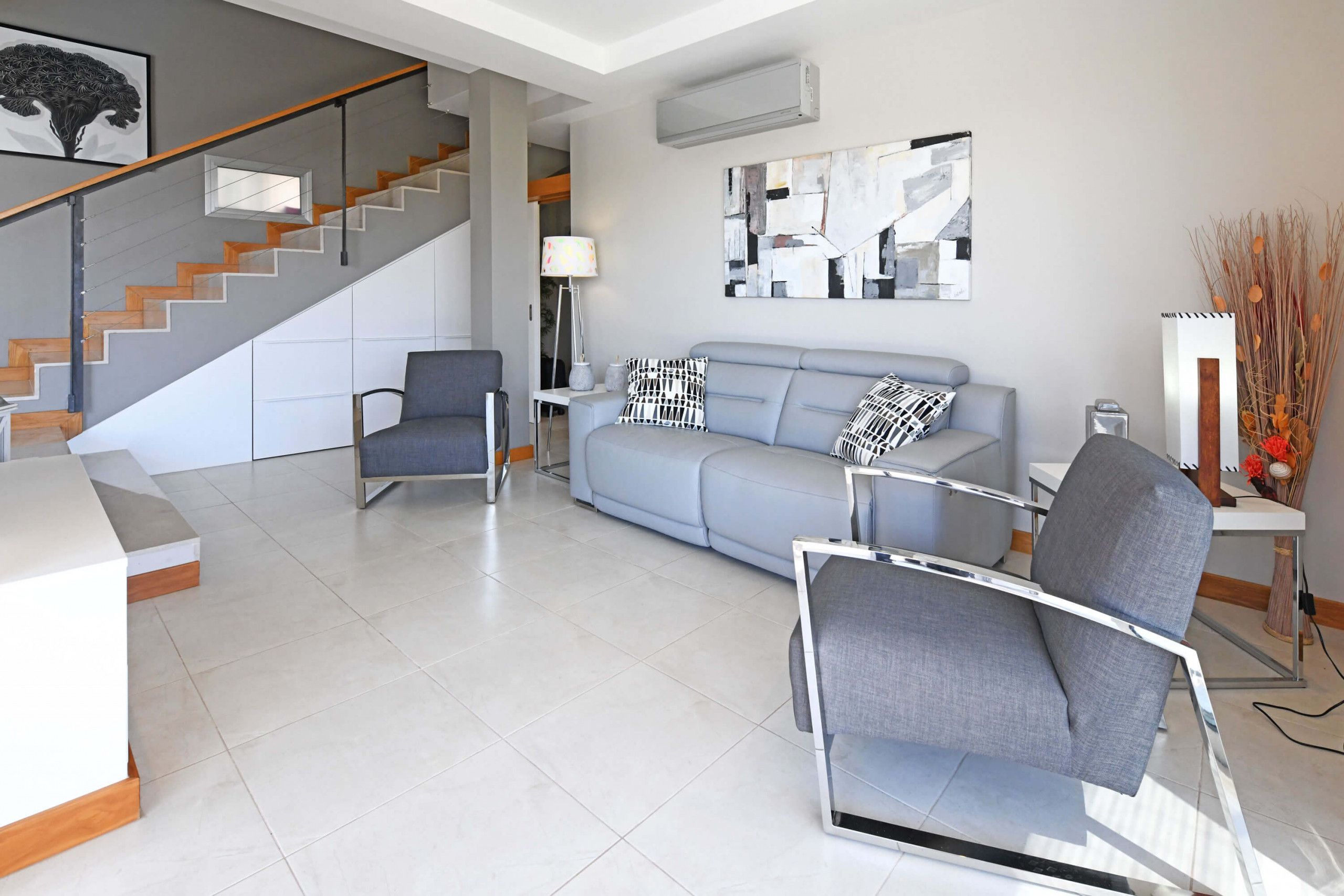 Ein modernes Wohnzimmer mit einem grauen Sofa, einem grauen Sessel und einer Treppe mit Holzstufen.
