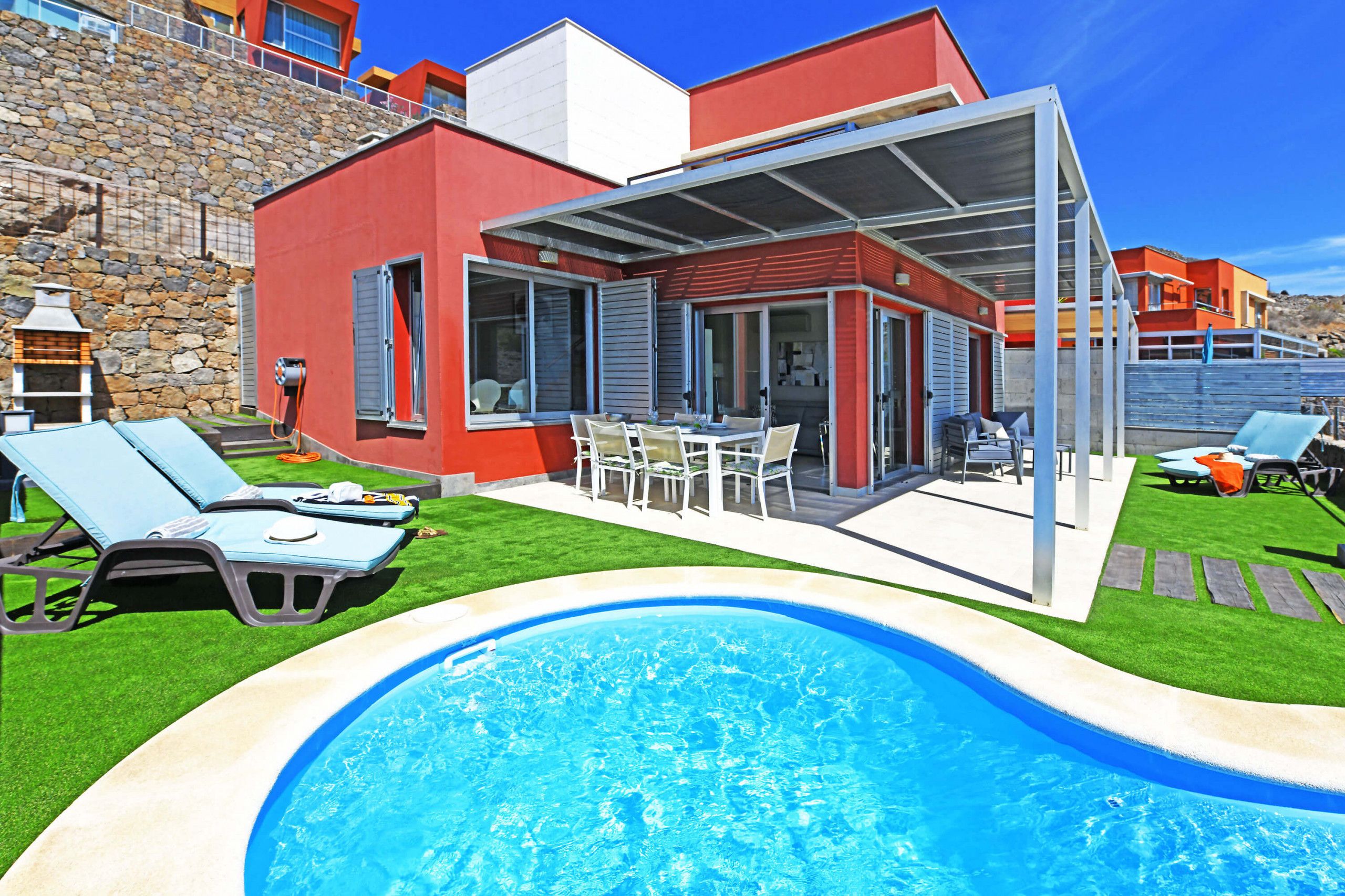 A modern house with a swimming pool, outdoor seating, and a stone wall.