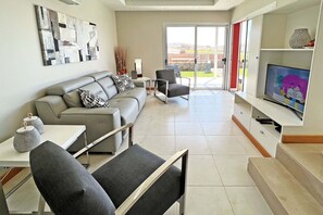 A modern living room with a grey sofa, a grey armchair, a small table with decorative items, and a television on a white stand.