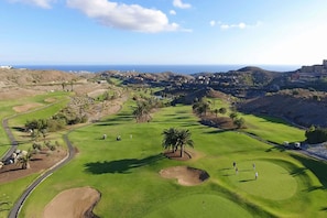 A golf course with a clear view of the ocean, palm trees, and a distant town. - Salobre Vista Golf 5 (San Bartolomé de Tirajana)