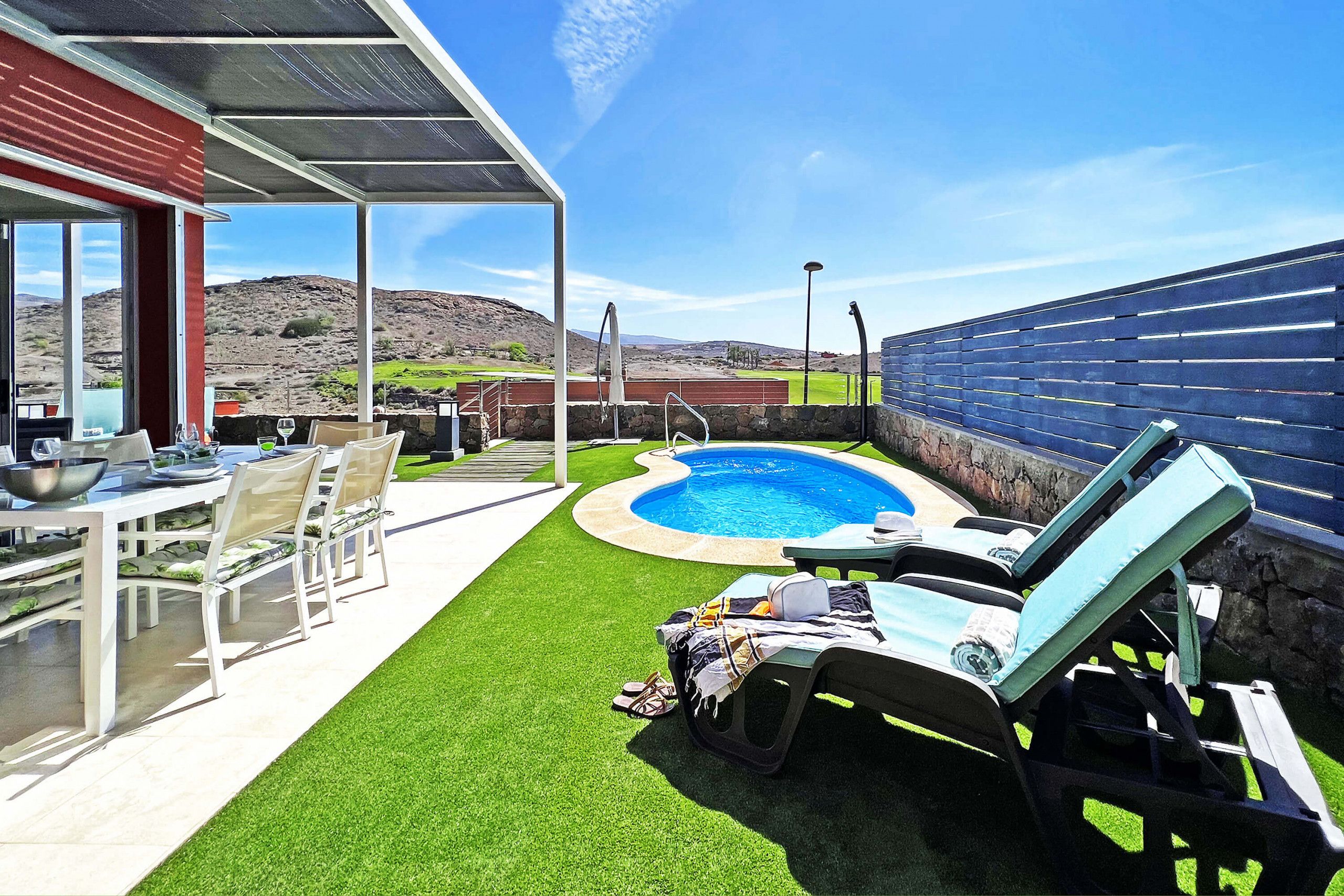 Un espace piscine avec un jacuzzi, un patio couvert doté d’une table et de chaises, et une vue sur un paysage montagneux.