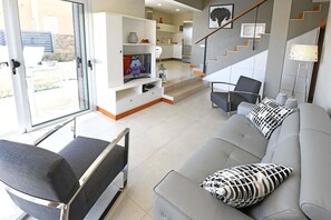 A modern living room with a grey sofa, a TV, and a staircase leading to an upper floor. - Salobre Vista Golf 5 (San Bartolomé de Tirajana)