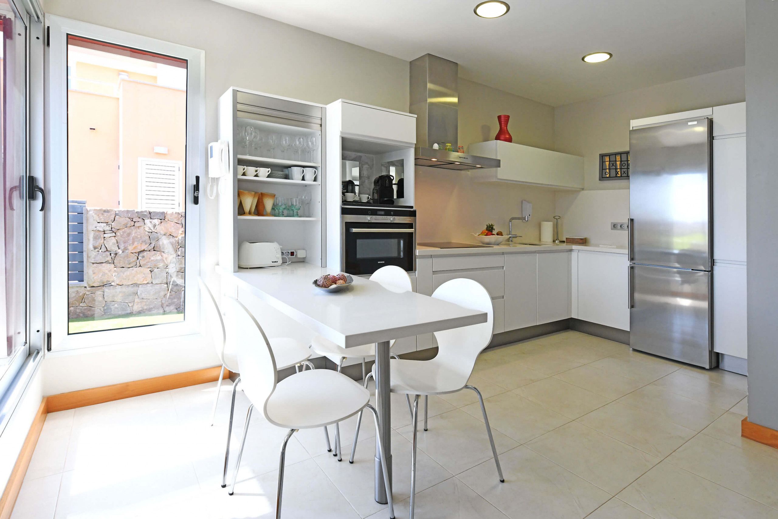 A modern kitchen with white cabinetry, a built-in oven, and a stainless steel refrigerator.