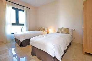 A hotel room with two beds, a window with curtains, a nightstand with a lamp, and a wooden wardrobe. - Salobre Morro Golf 6 (San Bartolomé de Tirajana)