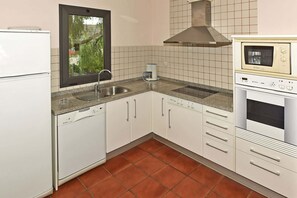 A kitchen with white cabinets, a dishwasher, a coffee maker, a microwave, and a window with a view of greenery. - Salobre Morro Golf 6 (San Bartolomé de Tirajana)