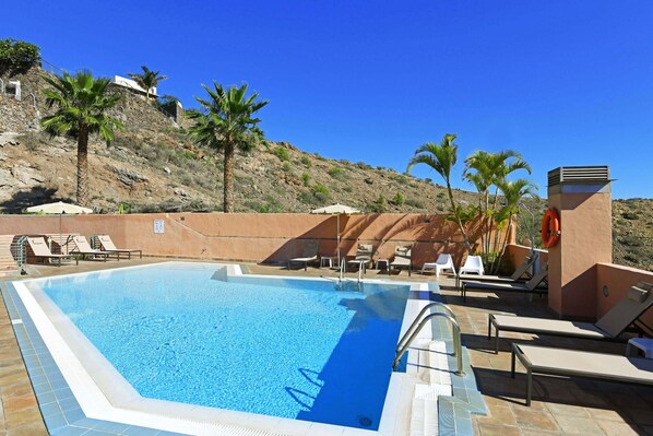 A swimming pool with lounge chairs and palm trees, surrounded by a hillside.