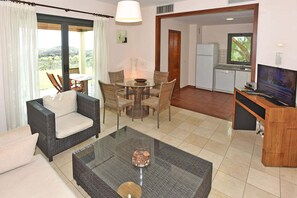 Ein Wohnzimmer mit Glastisch, Rattan-Sofa und Essbereich mit Stühlen.