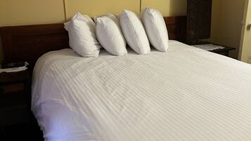 A neatly made bed with white linens and pillows, a framed picture on the wall, and two wall-mounted lamps.