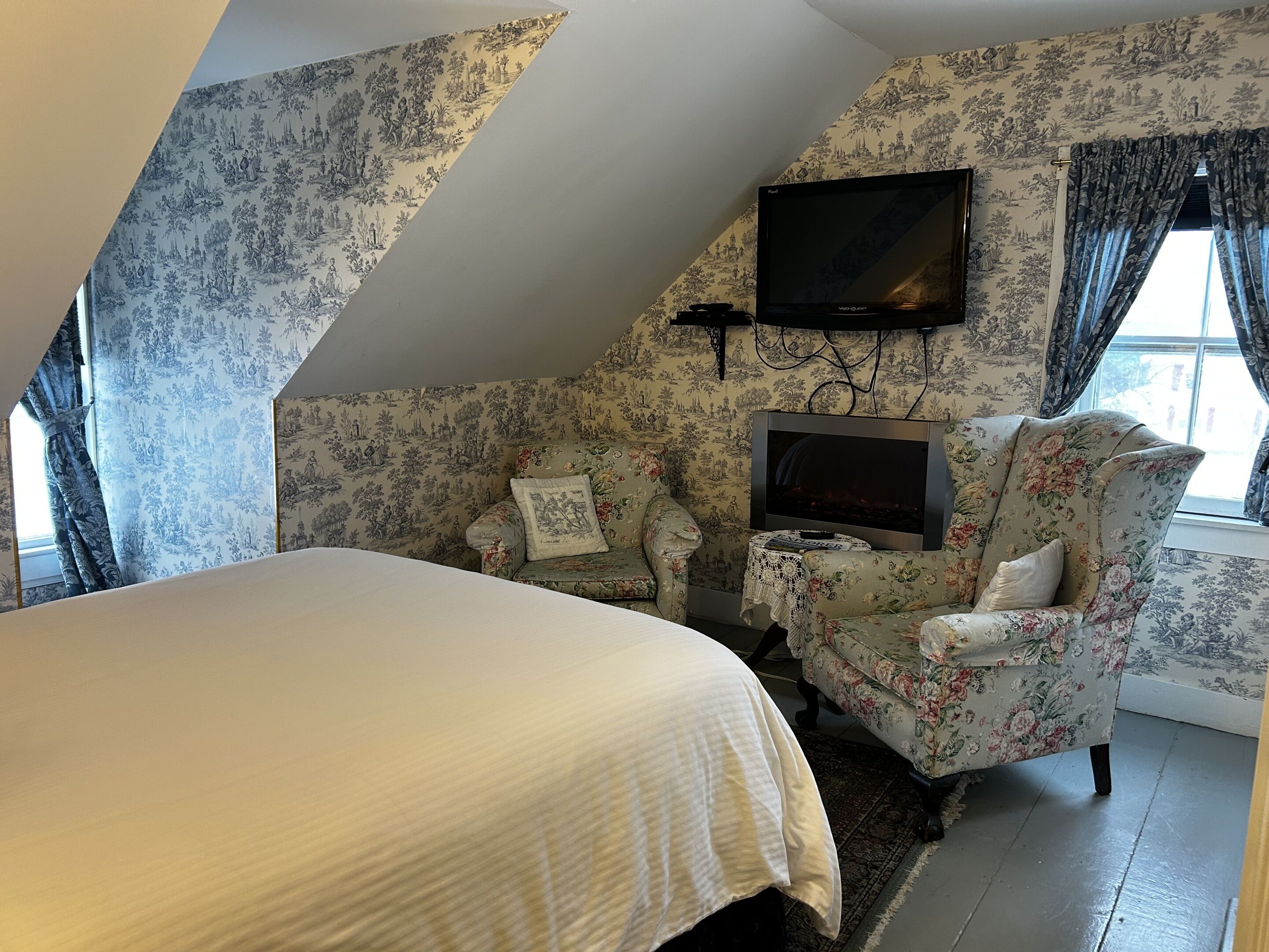 Een slaapkamer met een groot bed, een aan de muur bevestigde televisie en een bank met bloemenprint.