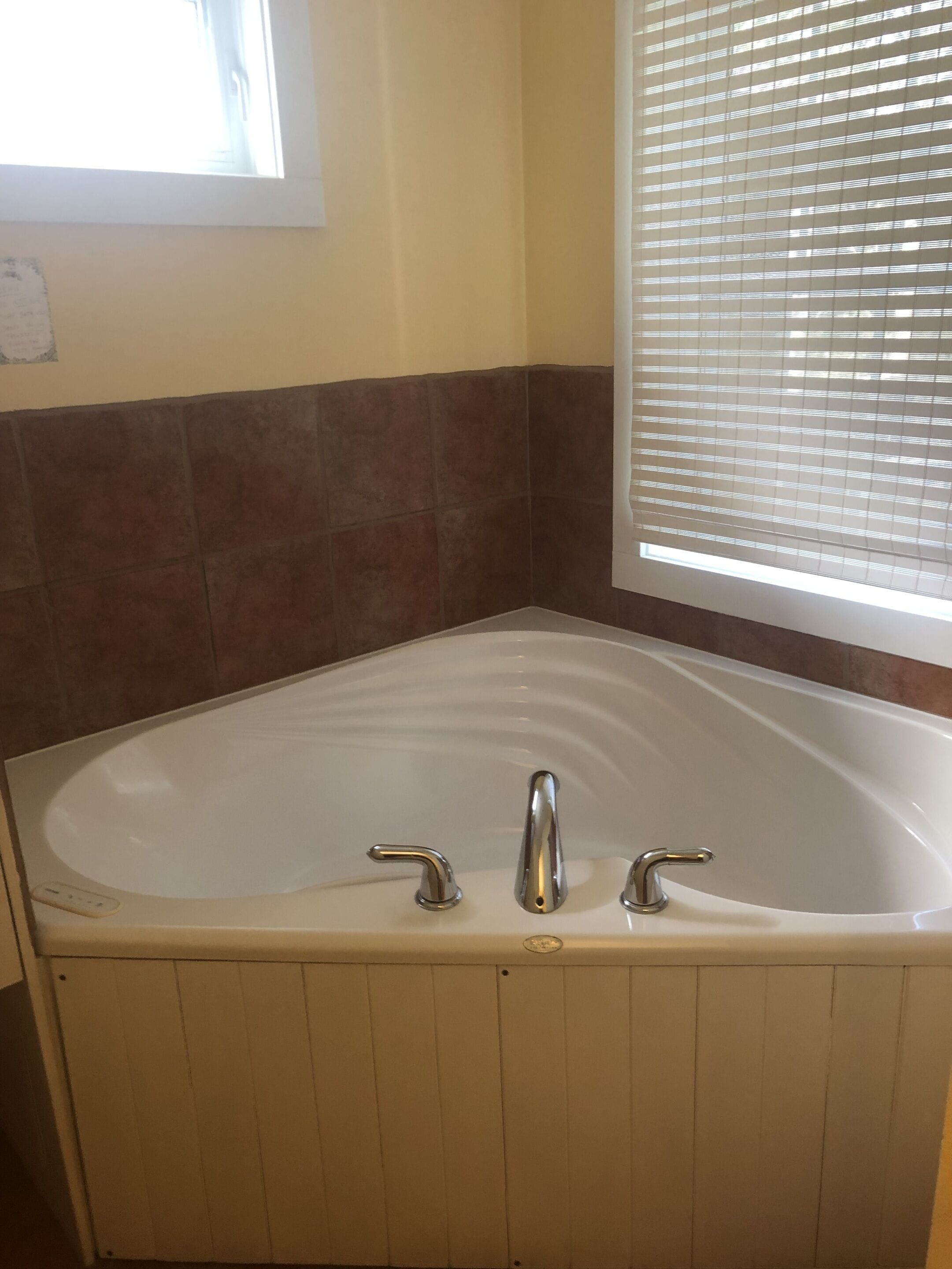 Un baño con una bañera independiente, una ventana con persianas y una pared con azulejos.