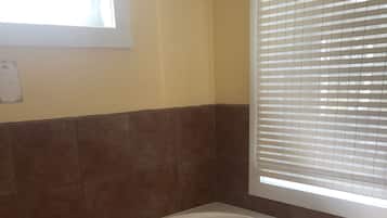 Un baño con una bañera independiente, una ventana con persianas y una pared con azulejos.