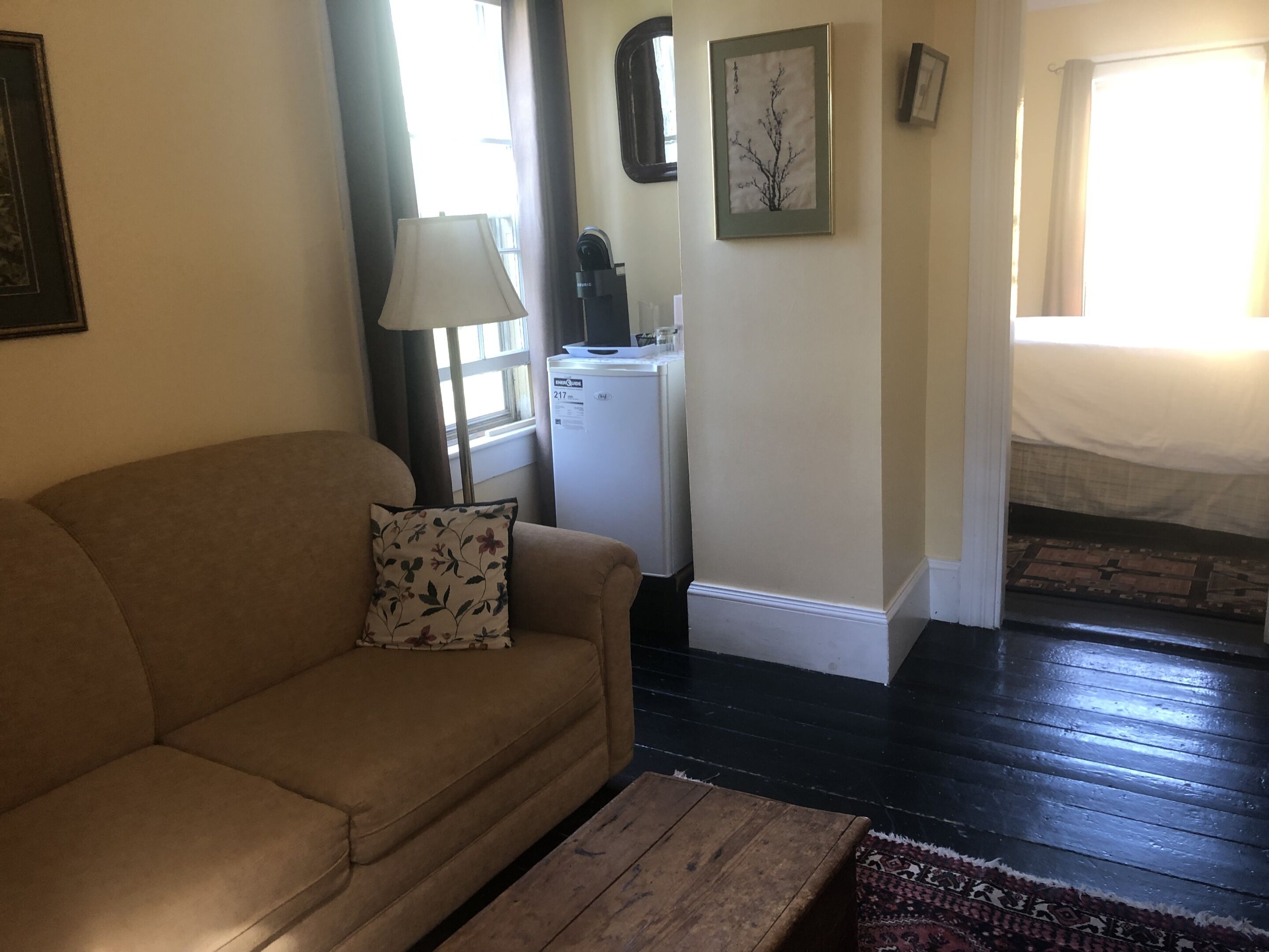 Un salon avec un canapé, une table basse, une lampe, un réfrigérateur et un tapis à motifs.