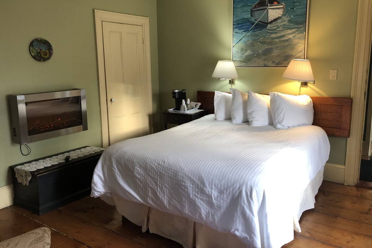 Una habitación de hotel con una cama, televisión, mesita de noche, un cuadro y suelo de madera.