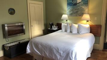 Una habitación de hotel con una cama, televisión, mesita de noche, un cuadro y suelo de madera.