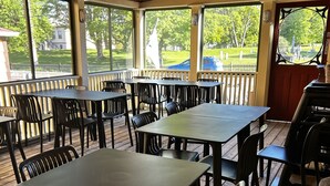 A covered patio area with tables and chairs, large windows, and a view of a cemetery. - The Garrison House Inn (Annapolis Royal)