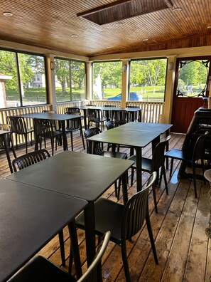 Un patio couvert avec des tables et des chaises, de grandes fenêtres et une vue sur un cimetière.