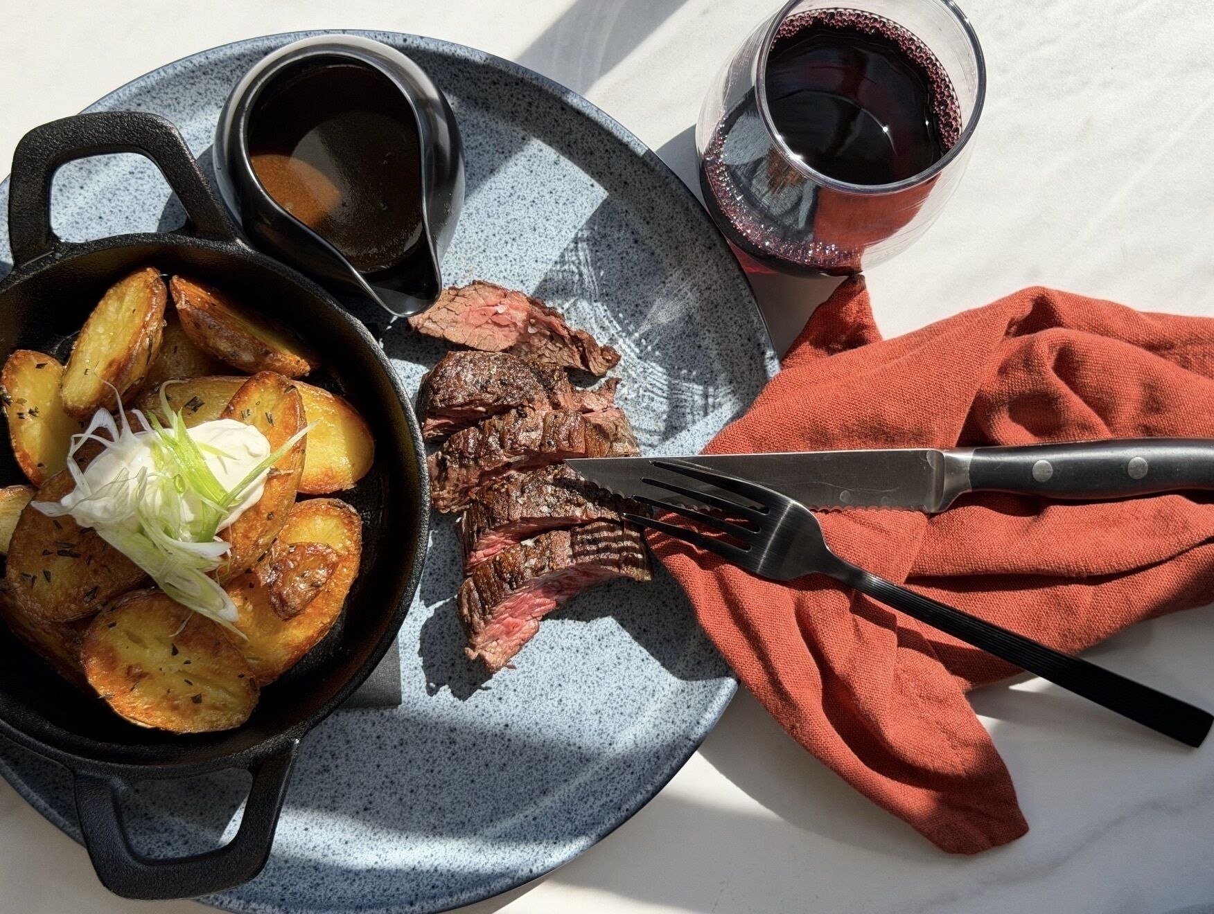 A meal with steak, roasted potatoes, and a glass of red wine on a plate.