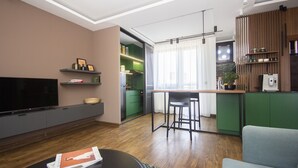 A modern living room with a flat-screen TV, a sofa, and a dining area with a kitchen in the background. - Cozy penthouse, terrace, artisan touch perfect espresso & perks (Belgrade)