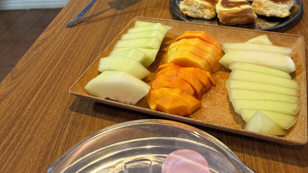A buffet table with various food items including pastries, bread, and sliced fruits.