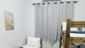 A room with two wooden bunk beds, a single bed, a white curtain, and a wall-mounted air conditioner.