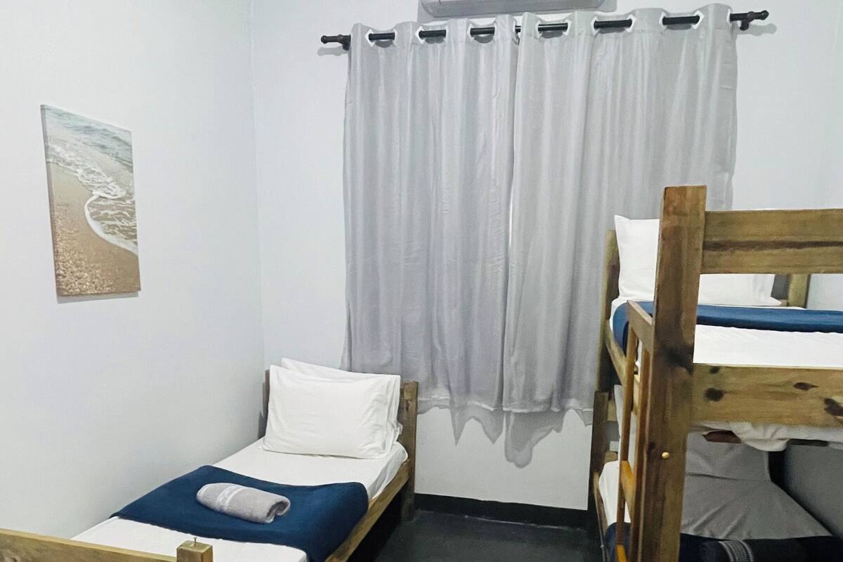 Una habitación con dos literas de madera, una cama individual, una cortina blanca y un aire acondicionado instalado en la pared.