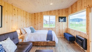 Una habitación acogedora tipo cabaña de madera, con cama, sofá, banco y chimenea.