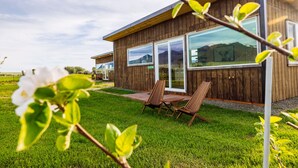 Una casa moderna de madera con ventanas amplias, un patio con sillas y un césped.