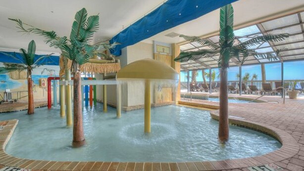 Ein Poolbereich im Innenbereich mit Palmen, einer Springbrunnen und einer Wandmalerei zum Thema Strand.