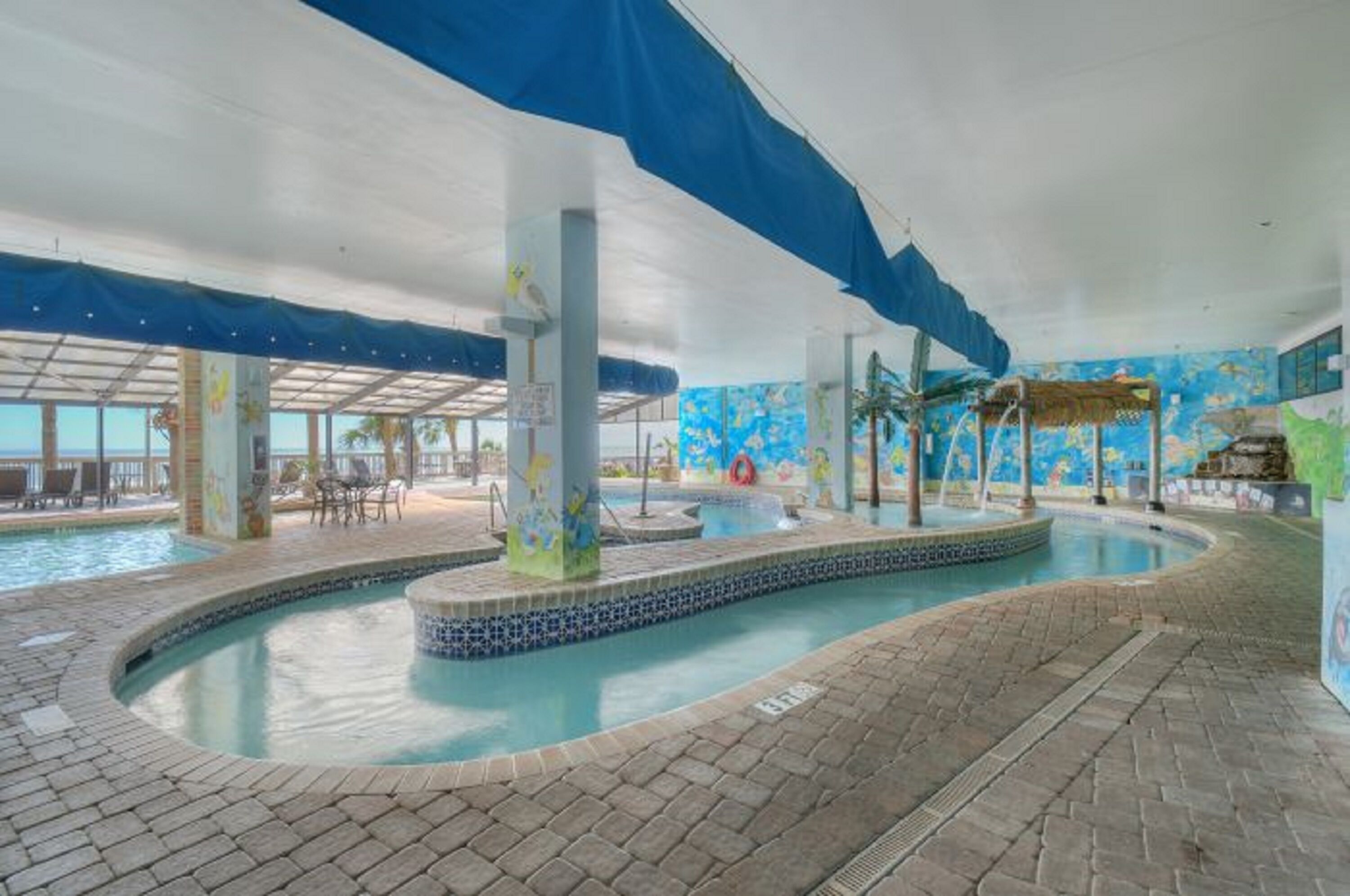 An indoor swimming pool with a tiled edge, a central fountain, and a mural on the wall.