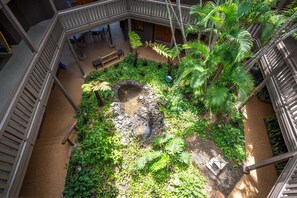 Un atrio de varios niveles con un elemento central de agua, rodeado de abundante vegetación y zonas de estar.