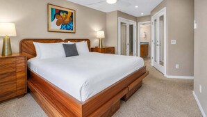 A bedroom with a wooden bed, two bedside tables with lamps, a ceiling fan, and a painting on the wall. - Oceanfront Hale Hui Kai 313 Large Lanai, AC, Incredible Views on Keawakapu Beach (Kihei)