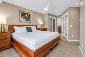 A bedroom with a wooden bed, two bedside tables with lamps, a ceiling fan, and a painting on the wall. - Oceanfront Hale Hui Kai 313 Large Lanai, AC, Incredible Views on Keawakapu Beach (Kihei)