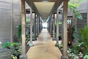 A covered walkway with a central path flanked by columns and greenery.