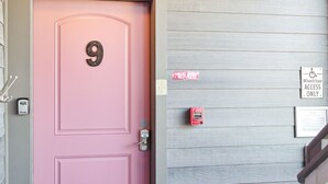 A pink door with the number 9, a fire alarm, a wheelchair access sign, and a light fixture above the door.
