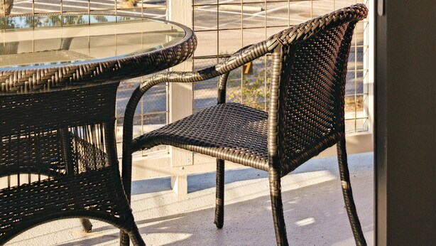 A balcony with wicker furniture overlooking a waterfront area with trees and a bridge.
