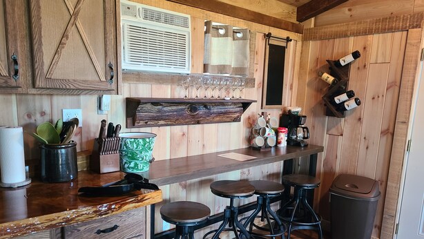 A kitchen with wooden cabinets, a bar area with stools, a wine rack, and a coffee station.