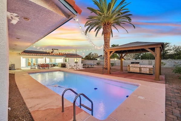Una piscina con un patio cubierto, una estación de barbacoa y una palmera.