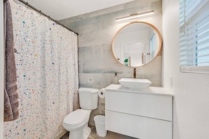 Un baño moderno con cortina de ducha, inodoro, lavabo y un espejo grande.