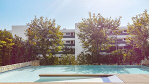 A swimming pool with a wooden deck, surrounded by trees and modern buildings. - Exquisite modern apartment [112] (Lagos)