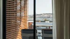 A view through a window with horizontal blinds, revealing a cityscape with buildings and a body of water in the distance. - Exquisite modern apartment [112] (Lagos)