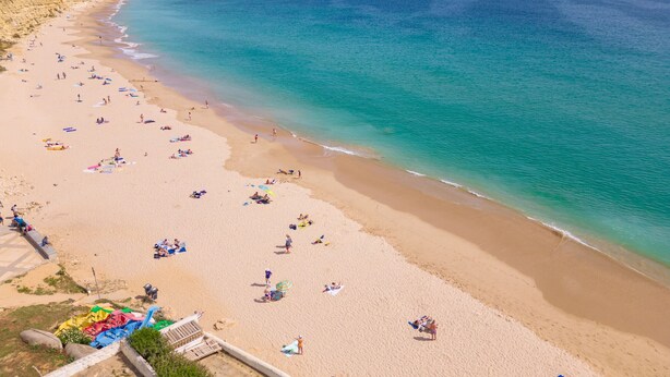 A beach with people sunbathing and swimming, a clear sky, and a calm sea. - Exquisite modern apartment [112] (Lagos)