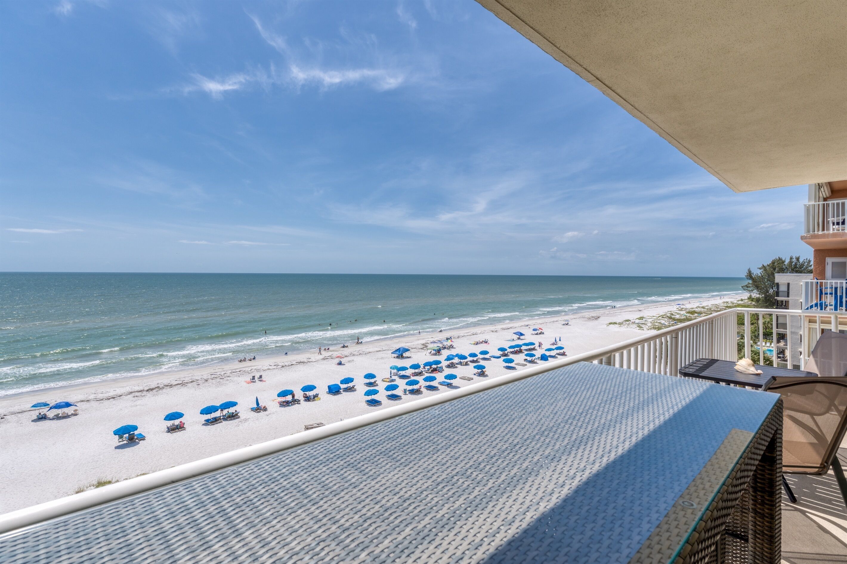 Un balcone con vista su una spiaggia, ombrelloni blu e cielo sereno.