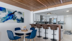 Eine moderne Küche mit weißen Schränken, einem Edelstahlkühlschrank und einer Holzzieldecke.