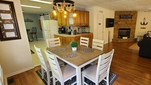 Un salon spacieux avec une cheminée, un coin repas avec une table et des chaises en bois, et une cuisine avec des meubles en bois et une machine à café.